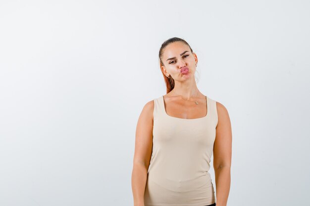 Young girl standing straight while posing, sending kisses in beige top, black pants and looking confident , front view.
