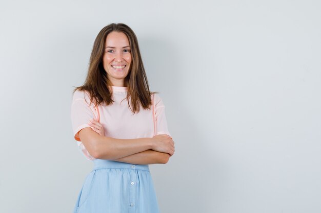 Young girl standing with crossed arms in t-shirt, skirt and looking cheerful , front view.