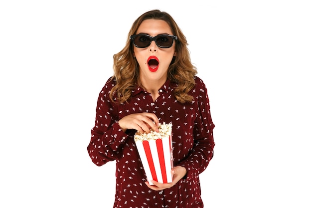 Young girl in stereo glasses holding popcorn and posing in surprise 