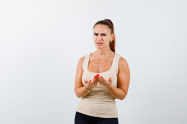 Young girl stretching cupped hands in beige top, black pants and looking disappointed