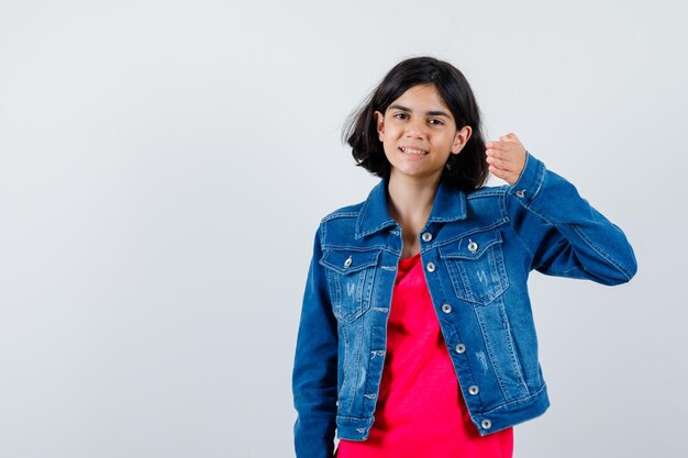 Young girl stretching hand toward camera in red t-shirt and jean jacket and looking optimistic. front view.