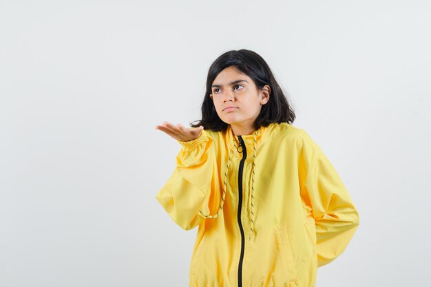 Young girl stretching hand toward camera in yellow bomber jacket and looking serious