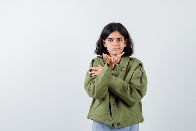 Young girl stretching hand toward in grey sweater, khaki jacket, jean pant and looking serious , front view.