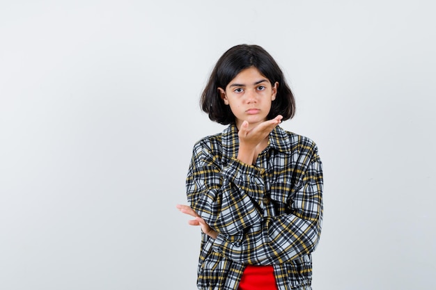 チェックのシャツと赤いTシャツで何かを持って、かわいく見えるように手を伸ばしている若い女の子。正面図。