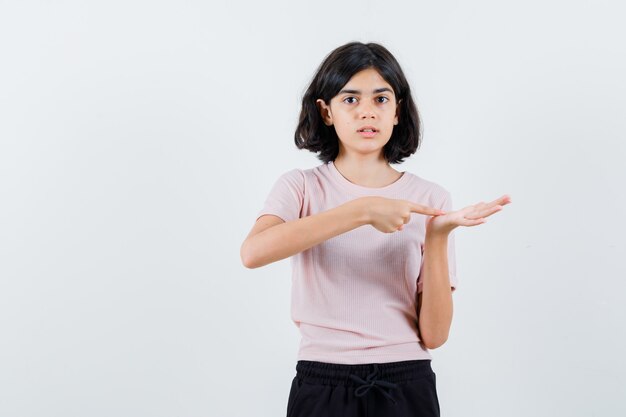 Young girl stretching hands as holding something imaginary and pointing to it in pink t-shirt and black pants and looking focused