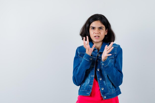 Young girl stretching hands as holding something in red t-shirt and jean jacket and looking harried