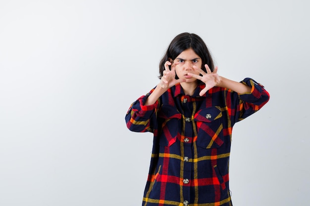 Young girl stretching hands as to menace someone in checked shirt and looking furious , front view.