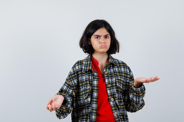 Young girl stretching hands in questioning manner in checked shirt and red t-shirt and looking perplexed , front view.