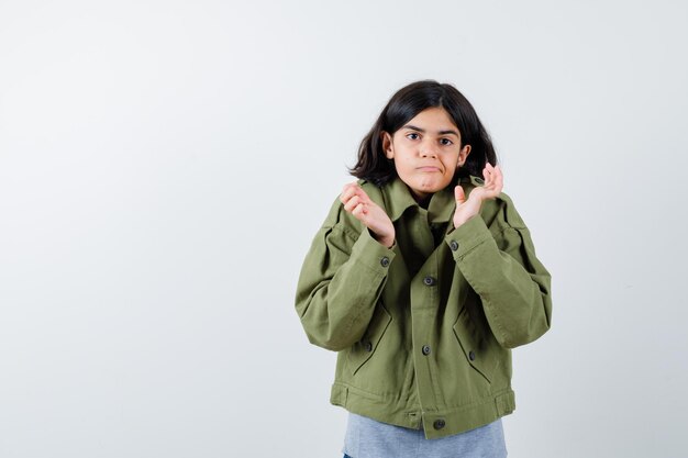 Young girl stretching hands in questioning manner in grey sweater, khaki jacket, jean pant and looking puzzled , front view.