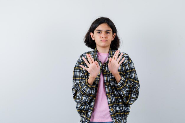 チェックシャツとピンクのTシャツに立ち寄るために手を伸ばして真剣に見える少女。正面図。