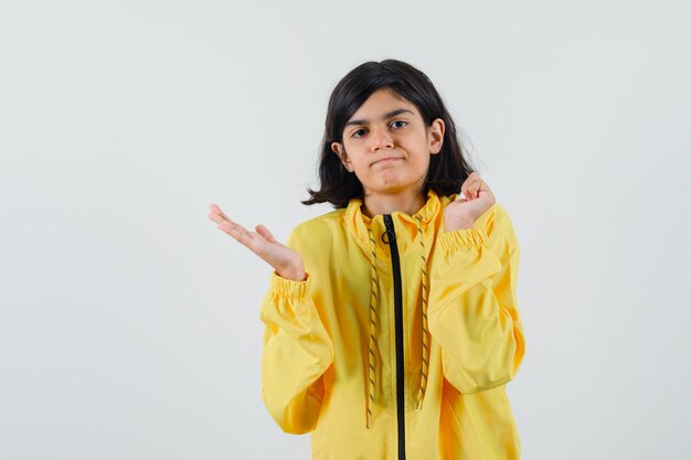 Young girl stretching one hand toward left, clenching fist in yellow bomber jacket and looking serious