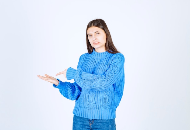 young girl in sweater pointing at hand on white.