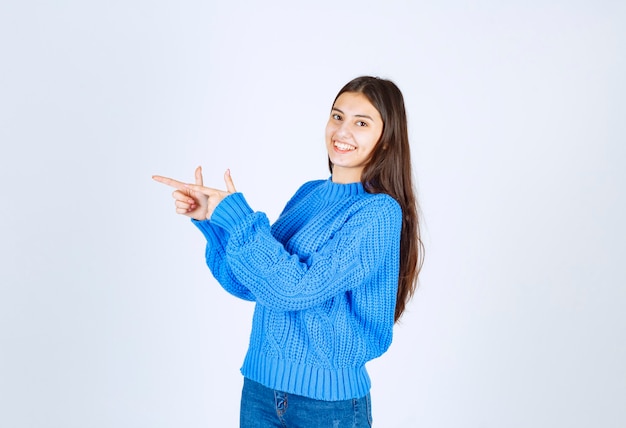 young girl in sweater pointing at her side on white.