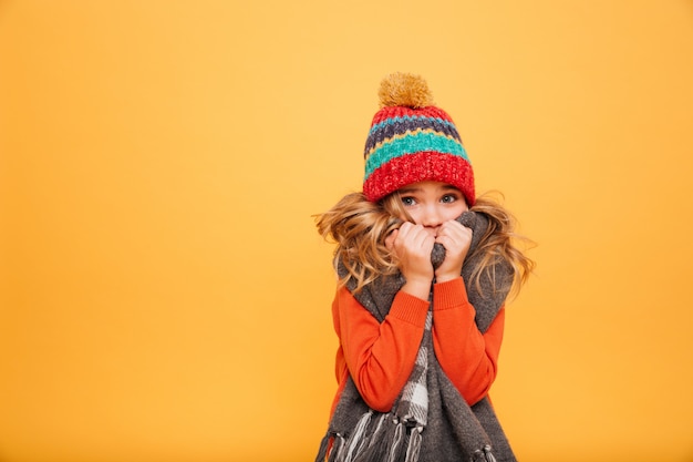 Молодая девушка в свитер, шарф и шапка с холодной, глядя на камеру над оранжевым