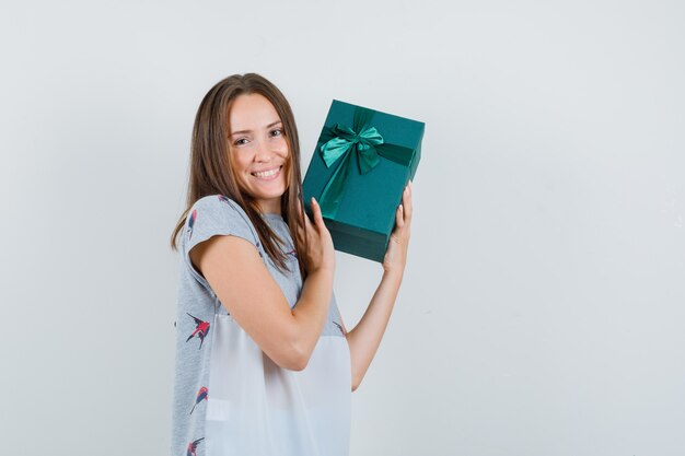 Young girl in t-shirt holding present box and looking glad , front view.