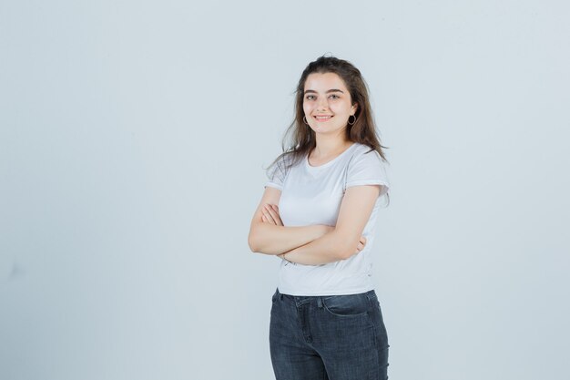 Young girl in t-shirt, jeans holding arms folded and looking pleased , front view.