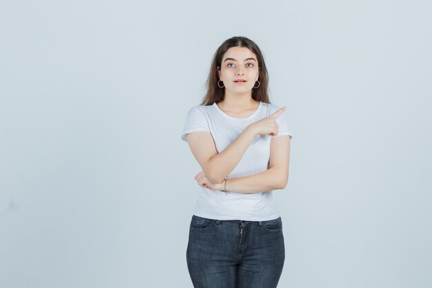 Young girl in t-shirt, jeans pointing aside and looking thoughtful , front view.