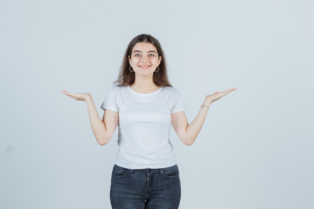 Young girl in t-shirt, jeans spreading palms out and looking happy , front view.