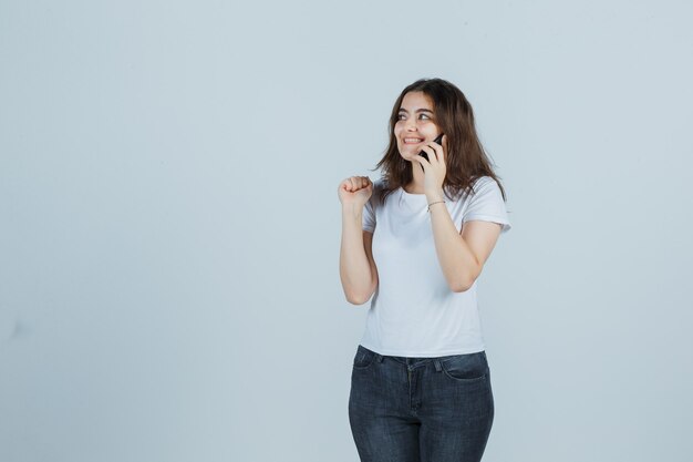 Tシャツを着た少女、携帯電話で話しているジーンズ、幸せそうに見える、正面図。