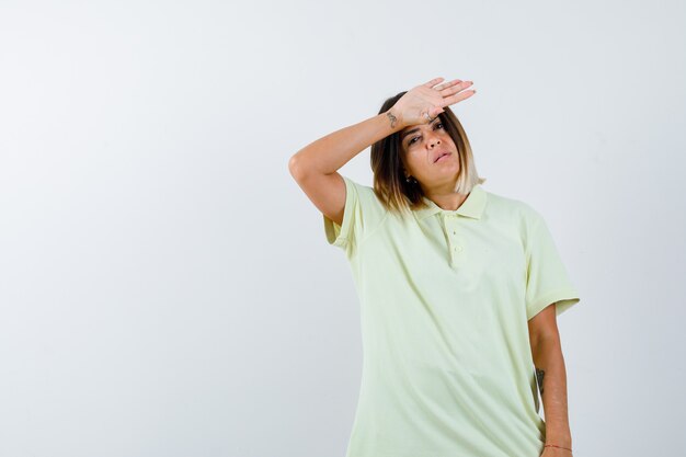 Young girl in t-shirt looking far away with hand over head and looking pensive , front view.