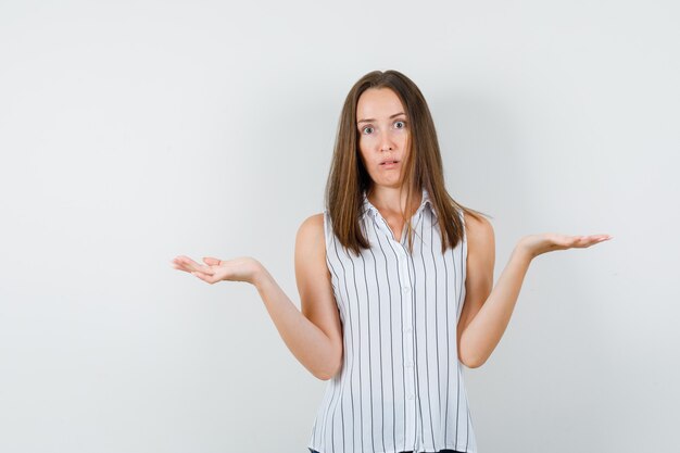 Young girl in t-shirt making scales gesture and looking puzzled , front view.