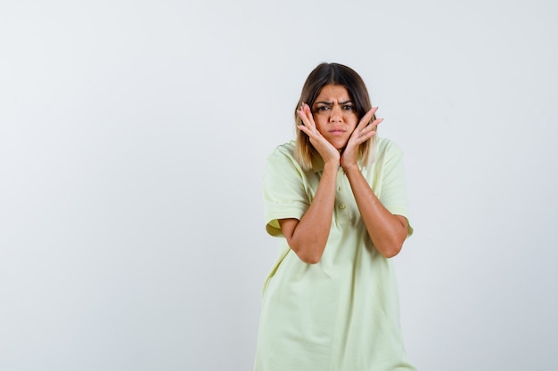 Young girl in t-shirt pillowing face on hands, grimacing and looking focused , front view.