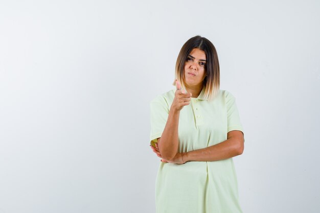 Young girl in t-shirt pointing at camera with index finger and looking serious , front view.