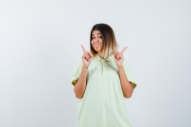 Young girl in t-shirt pointing up with index fingers and looking happy , front view.
