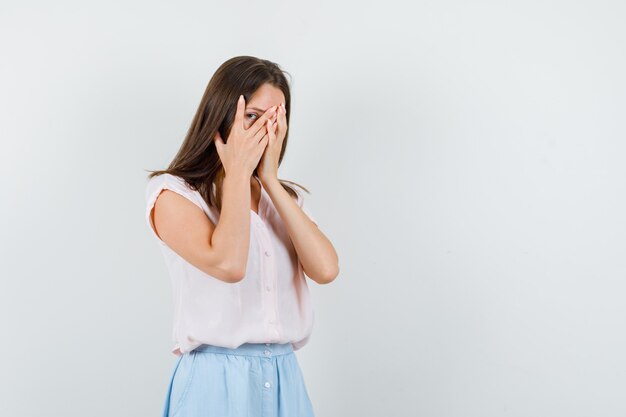 Young girl in t-shirt, skirt looking through fingers and looking scared , front view.