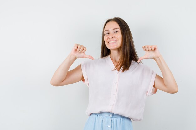 Tシャツを着た若い女の子、自分を指して自信を持って見えるスカート、正面図。