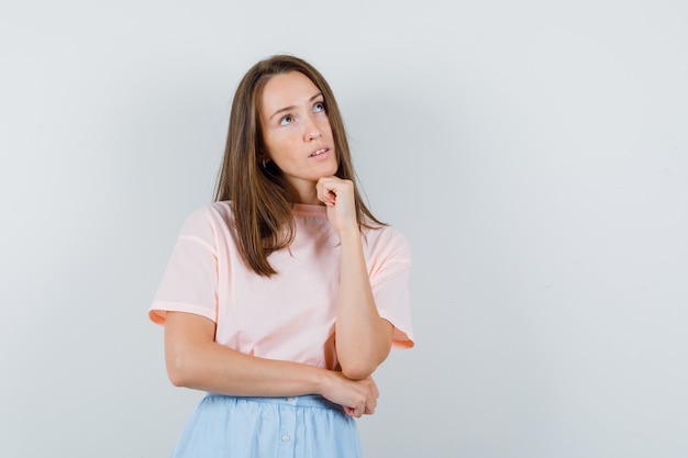 Young girl in t-shirt, skirt propping chin on fist and looking thoughtful , front view.