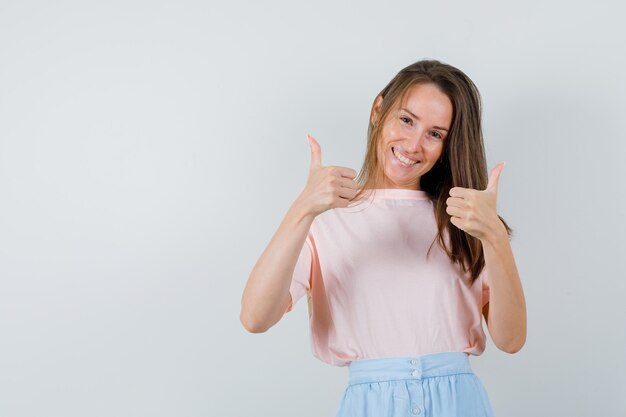 Молодая девушка в футболке, юбка показывает палец вверх и выглядит весело, вид спереди.
