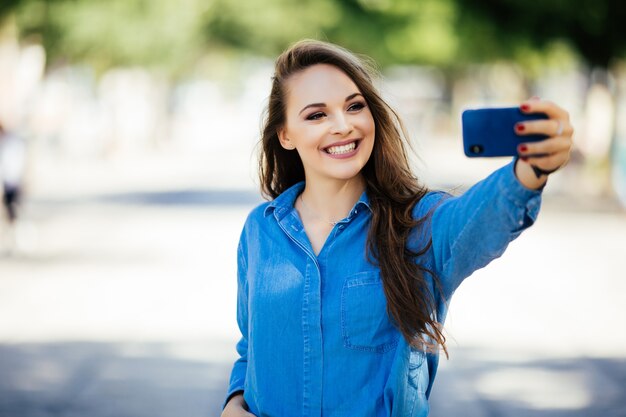 어린 소녀 여름 도시 거리에 전화로 손에서 selfie를 받아. 도시 생활 개념.