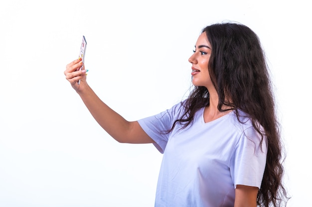 Young girl taking her selfie on the mobile phone on white wall