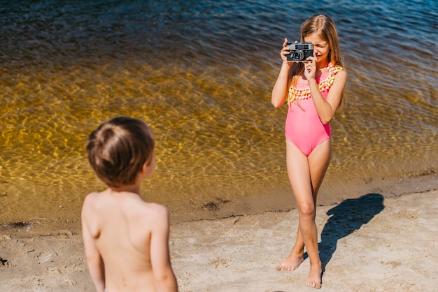 海のビーチの上に立って兄の写真を撮る少女