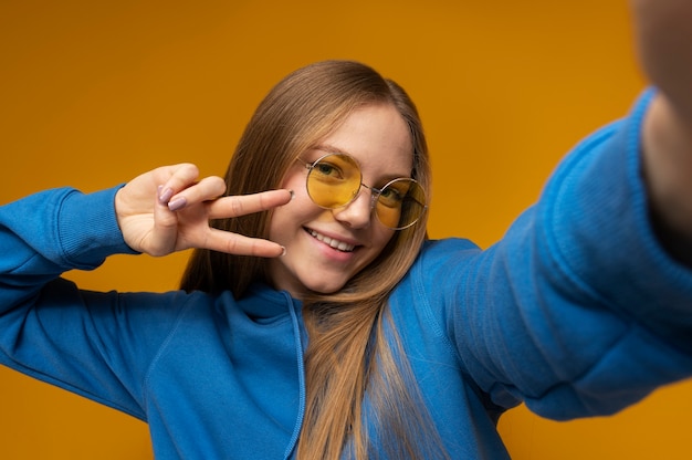 Free photo young girl taking a selfie while wearing sunglasses and showing the peace sign