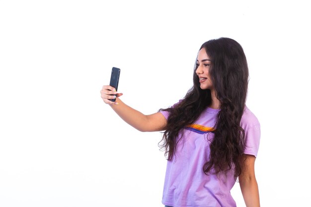 白い背景の上の彼女の携帯電話でselfieを取っている若い女の子