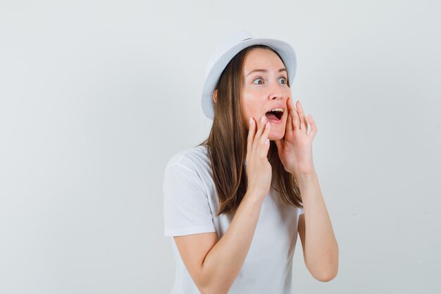 Young girl telling secret in white t-shirt hat and looking amazed  