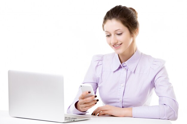 Young girl texting with smartphone in front of laptop