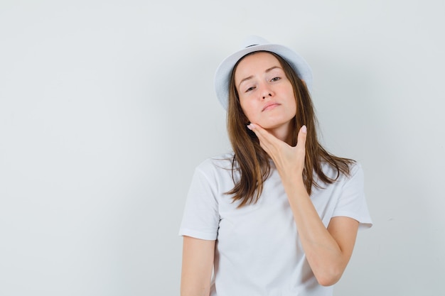 Young girl touching her chin in white t-shirt hat and looking elegant 