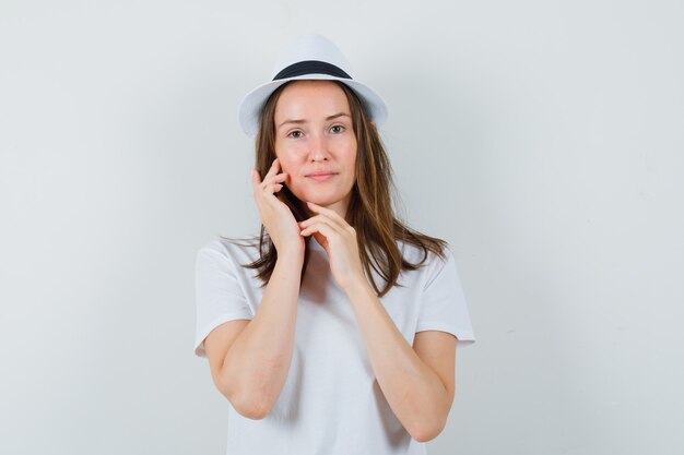 Young girl touching her face skin in white t-shirt hat and looking delicate  