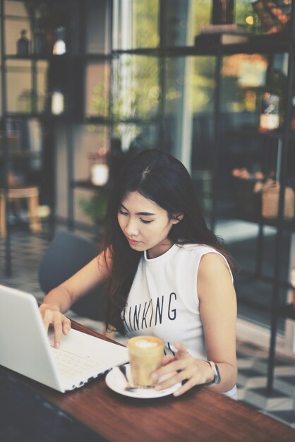 Young girl typing on her computer while having coffee