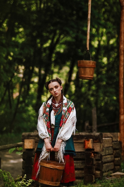 Young girl in a Ukrainian dress poses with a bucket near the well