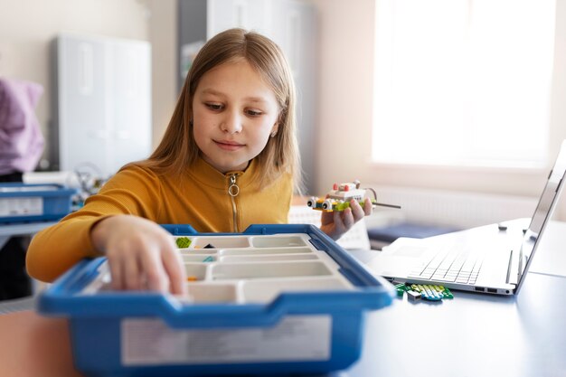 Молодая девушка использует ноутбук и электронные детали для сборки робота