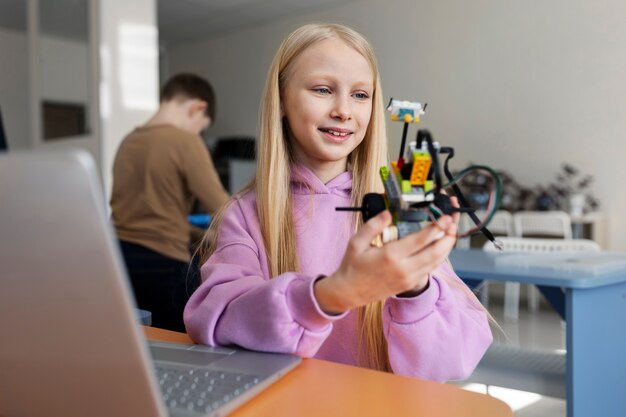 Young girl using a laptop and electronic parts to build a robot