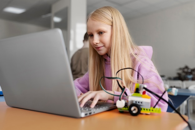 ノートパソコンと電子部品を使用してロボットを構築する少女