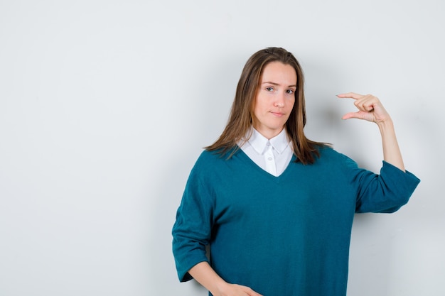 Giovane ragazza in maglione con scollo a v, camicia che mostra taglia piccola e sembra premurosa, vista frontale.