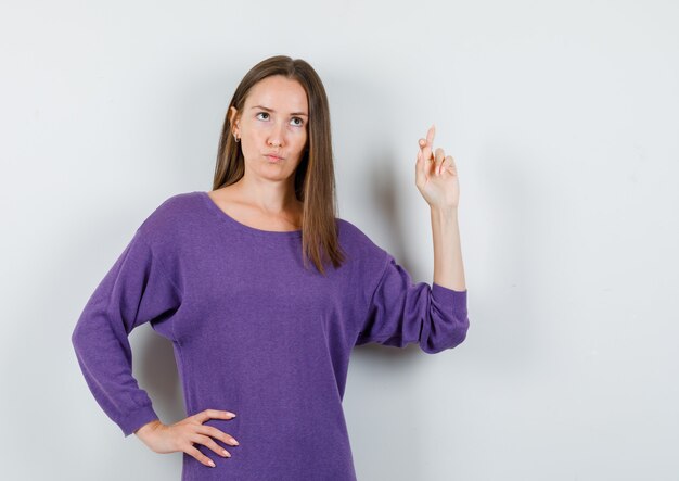 Young girl in violet shirt holding fingers crossed and looking pensive , front view.