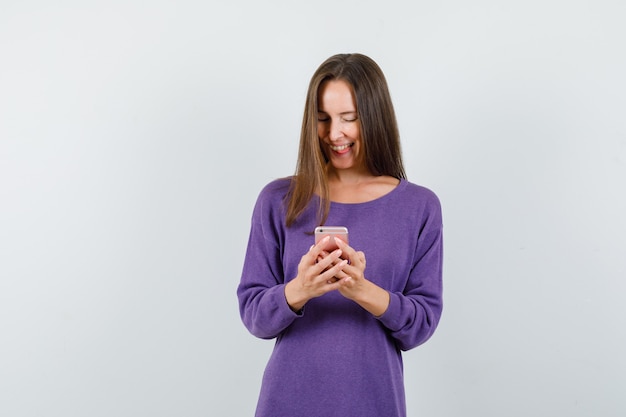 Young girl in violet shirt using mobile phone and looking cheerful , front view.