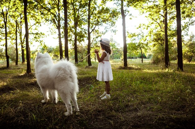 Young girl walking, playing with dog in park at sunset.
